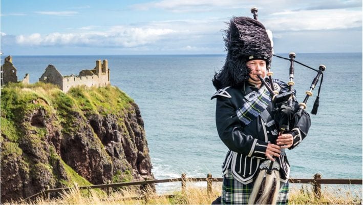 Scottish bagpiper playing near cliff in Scotland